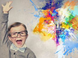 خلاقیت در کودکان- پسری عینکی با کت و پاپیون متعجب در طرف چپ تصویر و سمت راست لامپی که رنگهای مختلف در اطرافش پخش شده اند