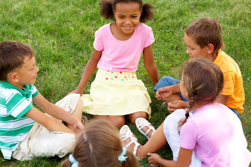چند کودک در کنار هم بر روی چمن نشسته اند و بازی می کنند. در حقیقت مهارت اجتماعی را برای آینده می آموزند.