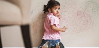 دروغ گویی در کودکان، کودکی مشغول نقاشی روی دیوار است و لباس صورتی رنگ و شلوار جین پوشیده و نگران در حال نگاه به پشت سرش است